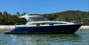 2004 Chris-Craft Roamer 43 Heritage Edition side profile at anchor off a beach, dark blue hull with hardtop
