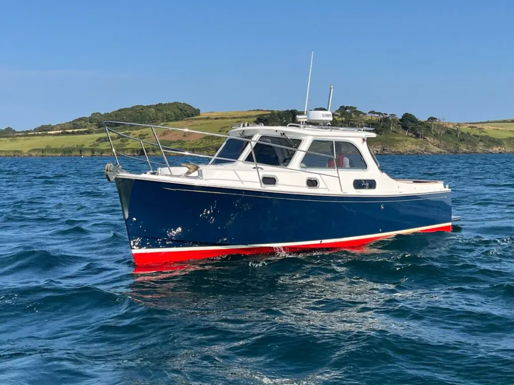 Duchy 27 'Zena', navy hull with red boot-top, running in open water with a green headland behind
