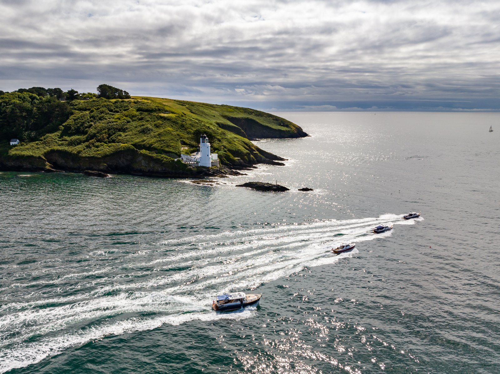 Aerial view of the Cockwells Owners' Rally 2022 fleet of Duchy Motor Launches and Hardy motor yachts leaving Falmouth across Carrick Roads