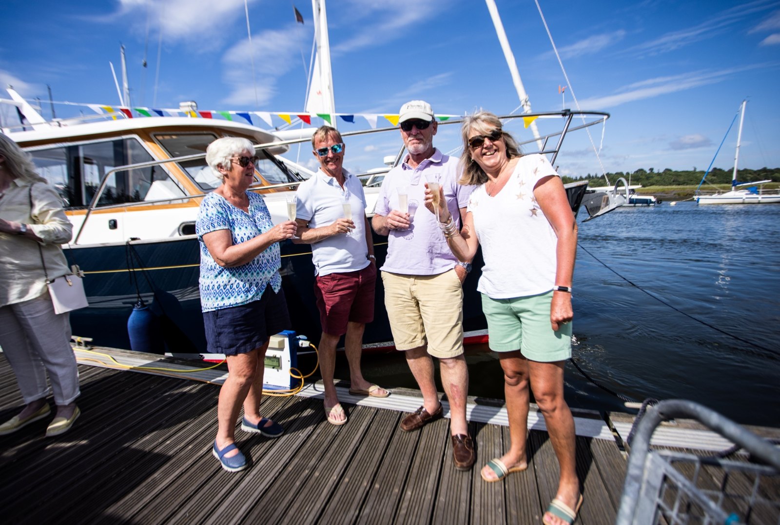Four rally guests with champagne on the pontoon at Buckler's Hard beside a navy-hulled Duchy 27 dressed with bunting