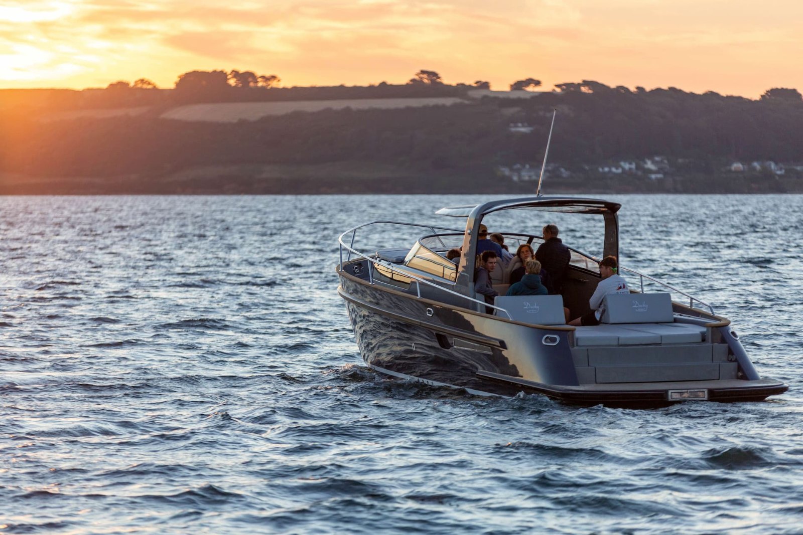 Duchy Sport at sunset with Bimini raised and guests in the cockpit, seen from the stern quarter