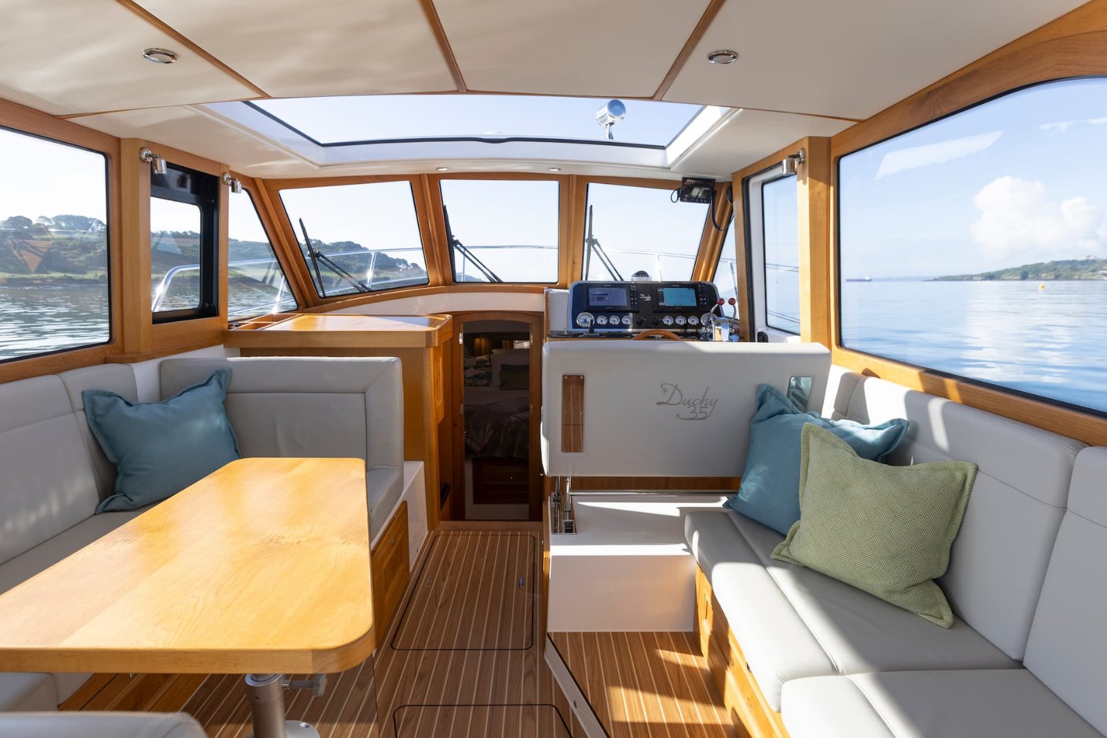 Oak-lined saloon of the Duchy 35 'Dolly' with the sunroof open, dining table and helm